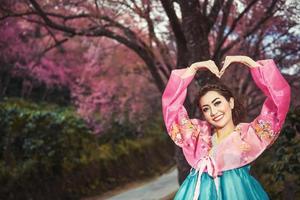 hanbok, das traditionelle koreanische kleid und das schöne asiatische mädchen mit sakura foto