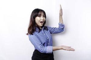 schockierte asiatische Frau mit blauem Hemd, die auf den Kopierbereich neben ihr zeigt, isoliert durch weißen Hintergrund foto