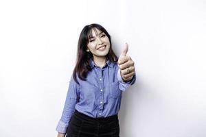 Aufgeregte asiatische Frau mit blauem Hemd gibt Daumen hoch Handgeste der Zustimmung, isoliert durch weißen Hintergrund foto