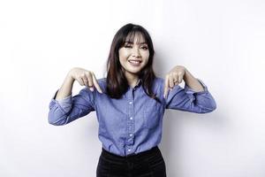 Aufgeregte asiatische Frau mit blauem Hemd, die auf den Kopierbereich zeigt, isoliert durch weißen Hintergrund foto