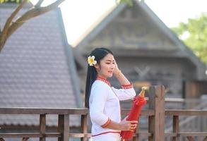 asiatische frau, die typisches thailändisches kleid mit rotem regenschirm trägt., thailändisches kostüm foto