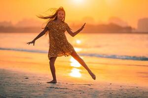 entzückendes glückliches kleines Mädchen am weißen Strand bei Sonnenuntergang. foto