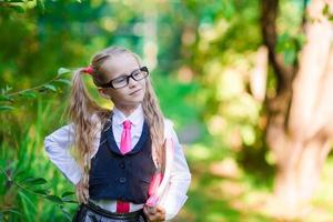 Porträt eines entzückenden kleinen Schulmädchens mit Notizen in einer Brille, die im Freien zur Schule geht foto