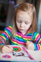 kleines süßes Mädchen, das mit Bleistiften malt, während es an ihrem Tisch sitzt foto