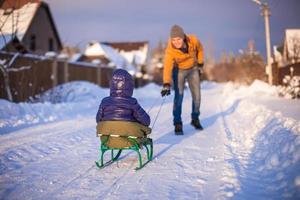 Junger Vater, der seine kleine Tochter auf einem Schlitten im Schnee im Freien schlitten foto