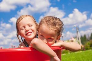 Zwei süße kleine glückliche Mädchen, die sich am Sommertag im kleinen Pool im Freien amüsieren foto
