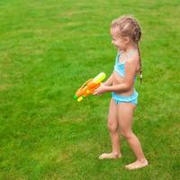Kleines entzückendes Mädchen, das an sonnigen Sommertagen mit Wasserpistole im Freien spielt foto