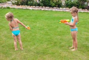 Zwei kleine entzückende Mädchen spielen mit Wasserpistolen im Hof foto