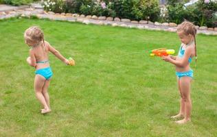 Zwei kleine entzückende Mädchen spielen mit Wasserpistolen im Hof foto