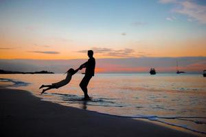 Kleines Mädchen und glückliche Vatersilhouette im Sonnenuntergang am Strand foto