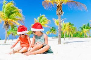 kleine entzückende mädchen in weihnachtsmützen während des strandurlaubs haben spaß zusammen foto