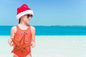 entzückendes kleines mädchen in weihnachtsmütze während der weihnachtsferien am strand foto