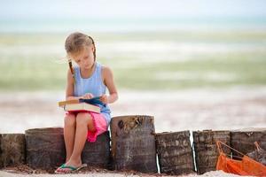Kleines entzückendes Mädchen mit Buch am tropischen weißen Strand foto