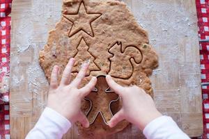 Kinderhände, die vom Teig-Lebkuchenmann für Weihnachten machen foto