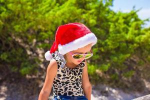 kleines Mädchen in der roten Weihnachtsmütze am weißen Strand im Freien foto