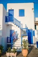 Typisches Haus mit blauen Balkonen, Treppen und Blumen. kleines Mädchen auf der Treppe im traditionellen griechischen Haus. schöne architektur gebäude außen mit kykladischem stil.