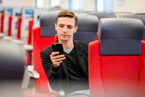 junger touristischer mann, der mit dem zug reist. Passagier, der während der Fahrt mit dem Schnellzug eine Nachricht auf dem Handy schreibt foto