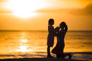 kleines Mädchen und glückliche Muttersilhouette im Sonnenuntergang am Strand foto