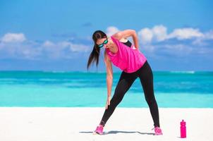 Gesunde Sportlerin, die in ihrer Sportkleidung am tropischen weißen Strand trainiert foto