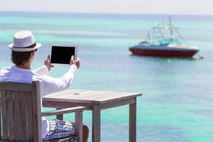 junger Mann mit Tablet-Computer im Café im Freien in den Sommerferien foto