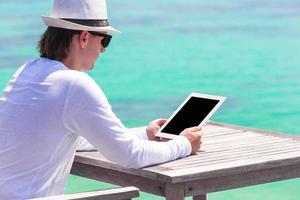 junger Mann mit Tablet-Computer im Café im Freien in den Sommerferien foto