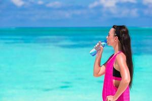 Fit junge Frau trinkt Wasser am weißen Strand foto