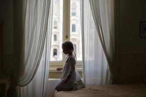 entzückendes kleines mädchen, das aus dem fenster auf duomo, mailand, italien schaut foto