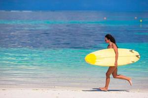 glückliche junge surffrau, die mit einem surfbrett am strand läuft foto