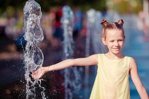 Kleines entzückendes Mädchen hat Spaß im Straßenbrunnen an heißen sonnigen Tagen foto