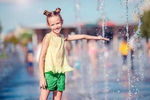 Kleines entzückendes Mädchen hat Spaß im Straßenbrunnen an heißen sonnigen Tagen foto