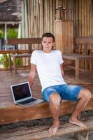 junger Mann mit Laptop im exotischen Resort im Freien foto