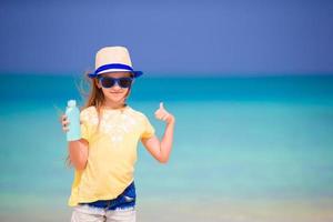 Kleines entzückendes Mädchen mit Sonnencremeflasche am Strand foto