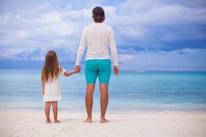 Rückansicht des kleinen Mädchens, das sich mit Papa am Strand umarmt foto