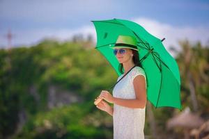 Mode junge Frau mit grünem Regenschirm, die am Meer spazieren geht foto