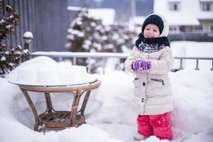 Kleines lustiges und fröhliches Mädchen, das sich am sonnigen Wintertag auf dem Hof amüsiert foto