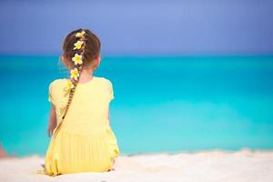 entzückendes kleines Mädchen mit Frangipani-Blüten im Haar am Strand foto