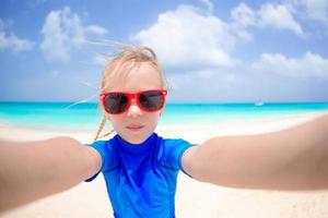 entzückendes kleines mädchen, das selfie am tropischen weißen strand macht foto