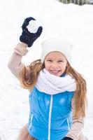 entzückendes kleines mädchen, das im winter draußen schneebälle spielt foto