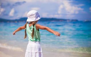 Rückansicht des schönen kleinen Mädchens breitete ihre Arme an einem exotischen Strand aus foto
