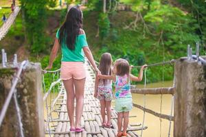 Rückansicht kleiner Mädchen und junger Frauen, die auf einer Hängebrücke über den Fluss Loboc, Philippinen, gehen foto