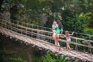 kleine mädchen und junge frau, die auf hängebrücke über den fluss loboc, philippinen, gehen foto