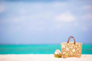 Closeup schöne Tasche mit Frangipani-Blüten und Kokosnuss am weißen Strand foto