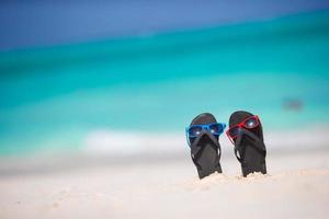 Sommer schwarze Flip-Flops mit Sonnenbrille am weißen Strand foto