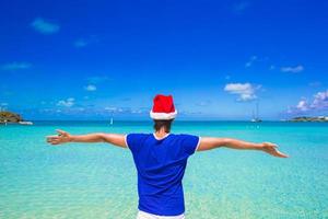 junger Mann in roter Weihnachtsmütze am tropischen Strand foto