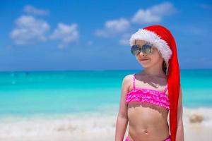 kleines süßes mädchen im roten hut weihnachtsmann am strand foto