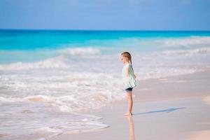 glückliches kleines Mädchen, das während des Karibikurlaubs am Strand spazieren geht foto