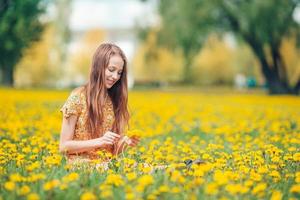 Kleines blondes Mädchen pflücken Blumen auf einer Wiese voller gelber Löwenzahn foto