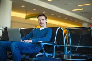 junger Mann mit einem Laptop am Flughafen, während er seinen Flug wartet foto