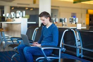 junger Mann mit einem Laptop am Flughafen, während er seinen Flug wartet foto