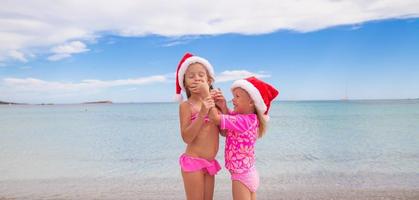 kleine entzückende mädchen in weihnachtsmützen während des strandurlaubs foto